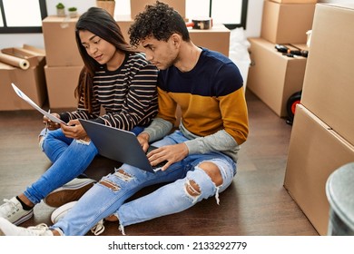 Young Latin Couple With Serious Expression Using Laptop Sitting On The Floor At New Home.