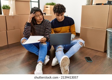 Young Latin Couple With Serious Expression Using Laptop Sitting On The Floor At New Home.