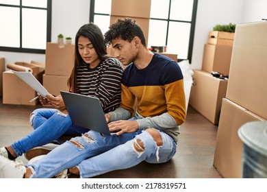 Young Latin Couple With Serious Expression Using Laptop Sitting On The Floor At New Home.