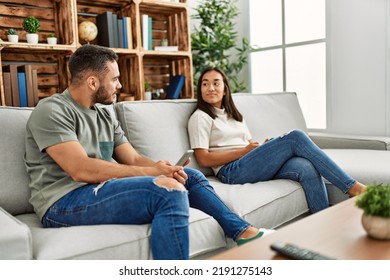 Young Latin Couple With Serious Expression Using Smartphone At Home.