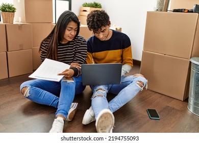 Young Latin Couple With Serious Expression Using Laptop Sitting On The Floor At New Home.