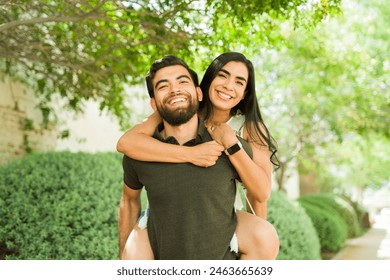 Young Latin couple sharing a playful piggyback ride on a sunny day, exuding happiness and affection during their outdoor date - Powered by Shutterstock