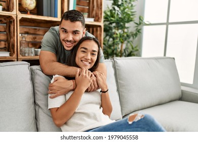 Young Latin Couple Sitting On The Sofa Hugging At Home.