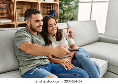 Young Latin Couple Smiling Happy Watching Tv At Home.