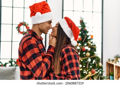 Young Latin Couple Smiling Happy And Hugging Standing By Christmas Tree At Home.