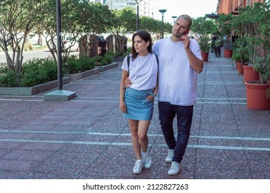 A Young Latin Couple Walking While The Man Talks On The Cell Phone.