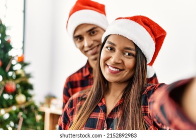 Young Latin Couple Wearing Christmas Hat Making Selfie By The Smartphone At Home.