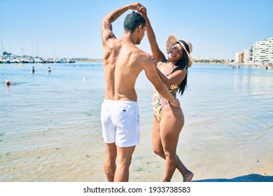 Young latin couple wearing swimwear  smiling happy and dancing at the beach.