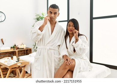 Young latin couple wearing towel standing at beauty center mouth and lips shut as zip with fingers. secret and silent, taboo talking 