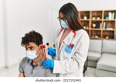 Young Latin Doctor Woman Wearing Medical Mask Auscultating The Ear Of Man Using Diapason At Examination Room.