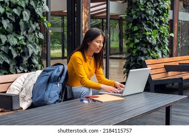 Young Latin Female Student Using Her Laptop On A Metal Table Outside