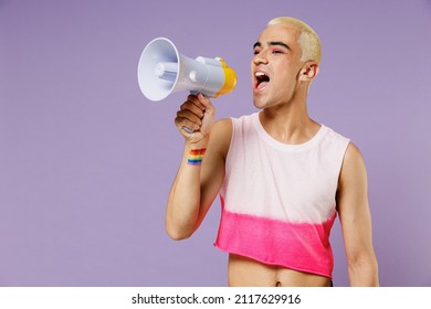 Young latin gay man with make up wearing bright pink top hold scream in megaphone announces discount sale Hurry up isolated on plain pastel purple background. People lifestyle fashion lgbtq concept