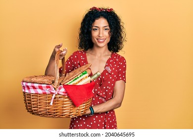 Young latin girl holding picnic wicker basket with bread smiling with a happy and cool smile on face. showing teeth. 