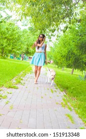 Young Latin Hispanic Brunette Woman Wear Blue Dress Walking With White Dog - Labrador Along The Path Laid Paving Stones Copy Space For Inscription 