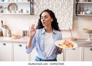 Young latin housewife tasting homemade pasta, gesturing and approving taste with closed eyes, enjoying delicious dish, standing in kitchen interior - Powered by Shutterstock