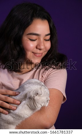 Young latin lady holding a gorgeous white scottish fold cat, with dark purple background