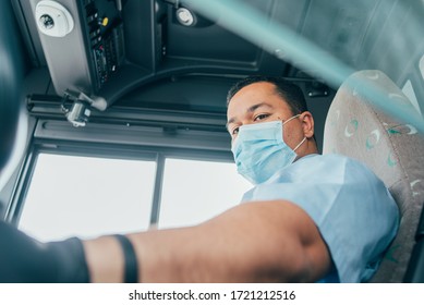 Young Latin Man Bus Driver In Blue Shirt Has Blue Medical Protection Mask And Black  Gloves On Hands To Protect Himself From Covid 19. Driver In Mask Looks In The Bus Mirror. Corona Virus Concept
