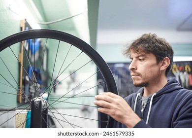 Young latin man checking the tension of the spokes of a bicycle wheel in his bike workshop. Real people at work. - Powered by Shutterstock