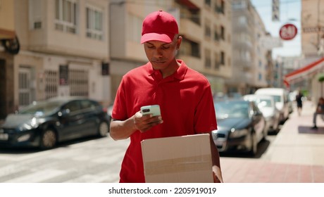 Young Latin Man Delivery Worker Scanning Package Using Smartphone At Street