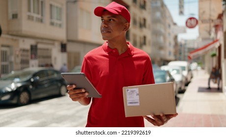 Young Latin Man Delivery Worker Holding Package Using Touchpad At Street