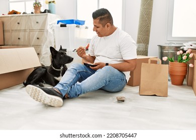 Young latin man eating taka away sushi food sitting on the floor at new home with dog. - Shutterstock ID 2208705447
