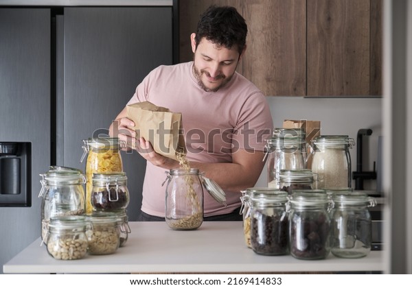 Young latin man filling up a jar with\
oat flakes from a paper bag. Food in bulk\
delivery.