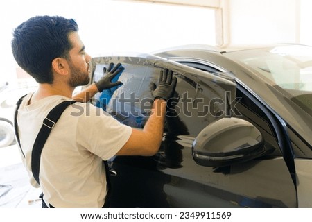 Young latin man installing tinting film on car window at auto detail service