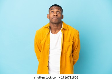 Young latin man isolated on blue background and looking up