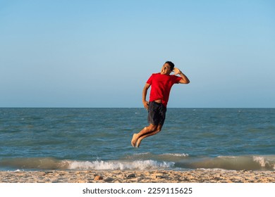 young latin man jumping on the shore of the beach - Shutterstock ID 2259115625