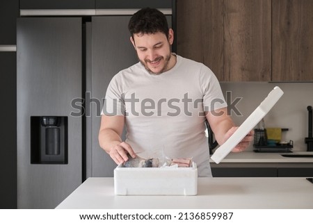 Young latin man opening his weekly delivery of fish in an EPS isothermal box, in the kitchen.