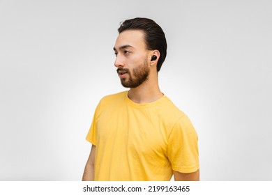 Young Latin Man In Profile With Ear Buds, Wireless Headphones, Looking To The Side With A White Background And Yellow Shirt.