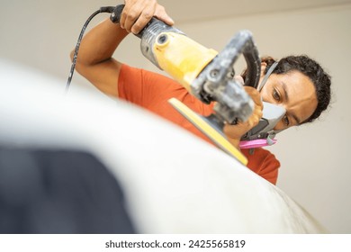 Young latin man with protective face mask polishing the edges of a surfboard in a shop - Powered by Shutterstock