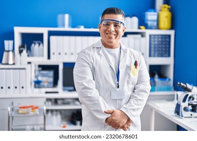 Científico latino joven sonriente confiado en estar de pie en el laboratorio