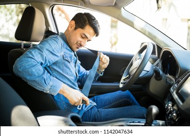 Young latin man sitting on car seat fastening seat belt