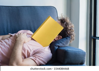 Young Latin Man Sleep On Sofa With Book Cover His Face, Sleep Late Reading Book Prepare For Exam. Lifestyle Education Concept