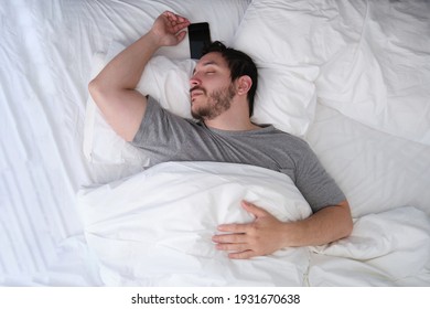 Young Latin Man Sleeping Spread Out In Bed With His Smartphone. Sleep Position Concept.