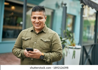 Young latin man smiling happy using smartphone at the city.