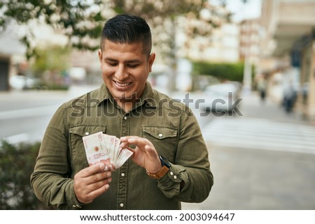 Young latin man smiling happy counting colombian pesos at the city.