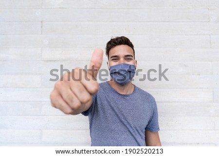 Young latin man with thums up while wearing protective face mask for coronavirus outbreak