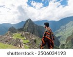 young latin man with typical poncho looking at the fortress of Machu Picchu in Cusco Peru