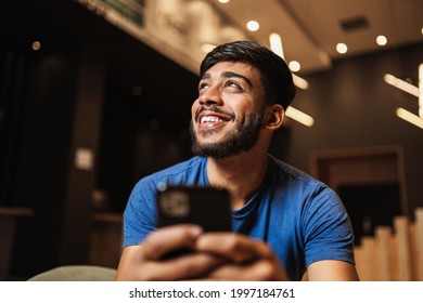 Young Latin Man Using Cell Phone. Texting On Cafe.