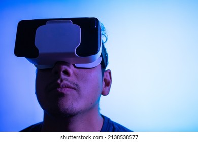 Young Latin Man Using Virtual Reality VR Headset 3D Glasses. Studio Blue Screen Backdrop. Low Key. 