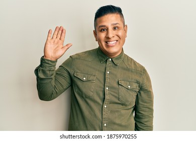 Young latin man wearing casual clothes waiving saying hello happy and smiling, friendly welcome gesture 