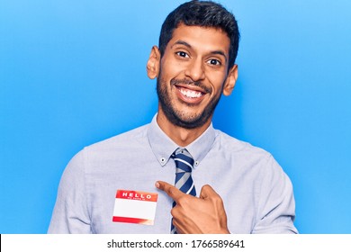 Young latin man wearing sticker with hello my name is message smiling happy pointing with hand and finger 