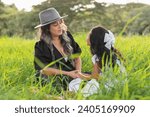 young latin mother chatting with her daughter while they spend their time sitting in a field of tall grass