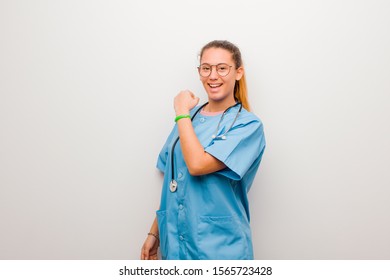 young latin nurse feeling happy, positive and successful, motivated when facing a challenge or celebrating good results against white wall - Shutterstock ID 1565723428