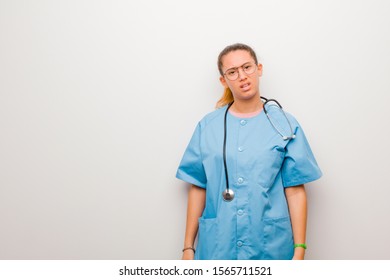 young latin nurse feeling puzzled and confused, with a dumb, stunned expression looking at something unexpected against white wall - Shutterstock ID 1565711521