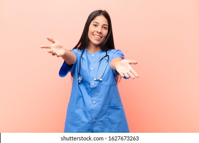 Young Latin Nurse Smiling Cheerfully Giving A Warm, Friendly, Loving Welcome Hug, Feeling Happy And Adorable Against Pink Wall