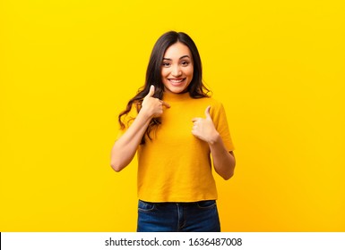 young latin pretty woman feeling happy, surprised and proud, pointing to self with an excited, amazed look against flat wall