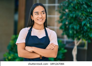 Young latin shopkeeper girl with arms crossed smiling happy at the city